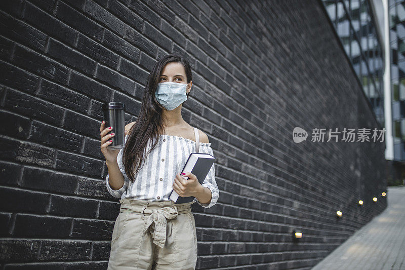 快乐年轻美丽的女学生拿着书和咖啡杯孤立在青砖背景