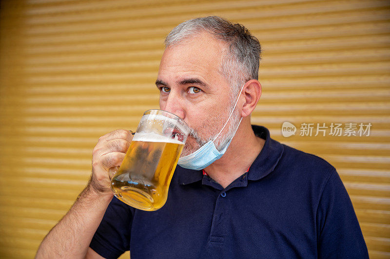 成熟的男人喝啤酒，并在下巴下面戴上保护面罩