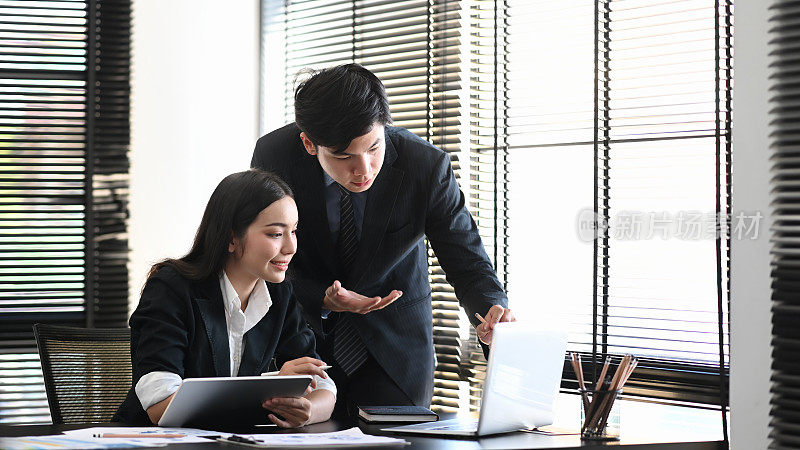 在现代的办公室里，熟练的年轻男员工向他的女同事解释一个显示在台式电脑显示器上的商业分析。