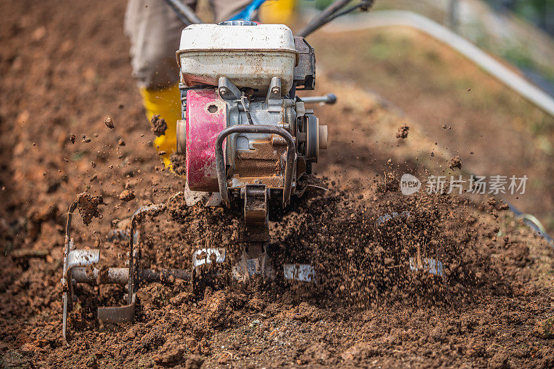 近距离观察，亚洲男性农民正用手摇拖拉机在山坡上犁地