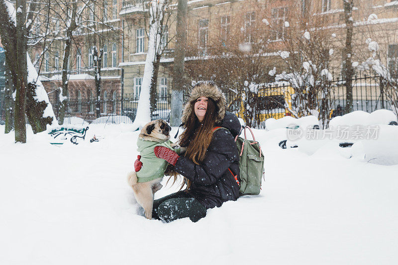 快乐的年轻女子背包享受第一雪在公园散步与小可爱的狗