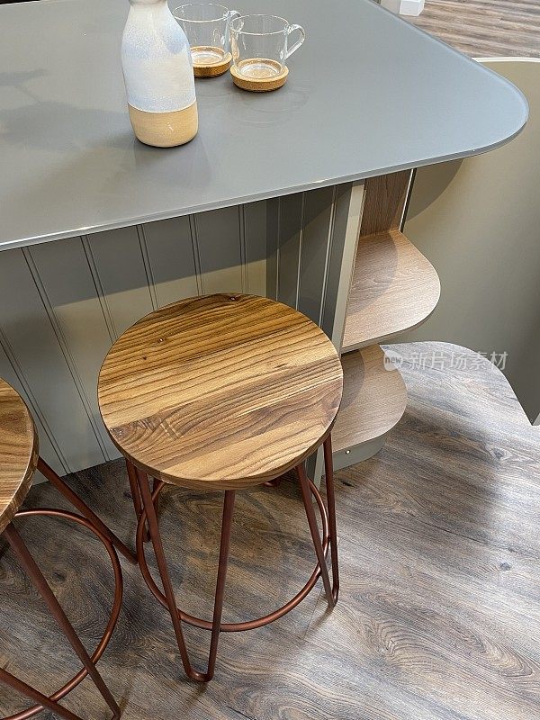 弯曲的厨房地板柜漆成鸭蛋蓝，早餐吧，舌槽包层木材，灰色复合可耐材料台面，橡木木凳与铜色金属腿，深色橡木效果强化地板