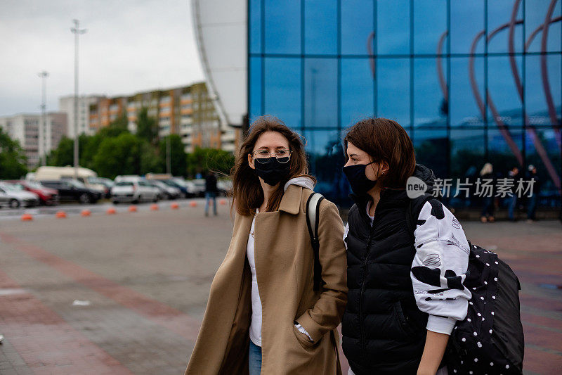 新常态两名妇女一起带医用防护口罩。女孩们在街上走着。新型冠状病毒和户外隔离概念。社会距离