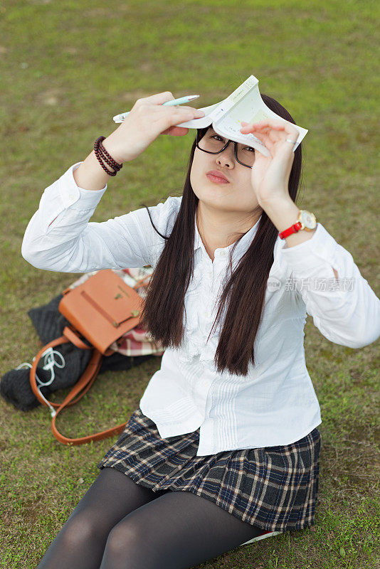 年轻的亚洲女孩拿着书坐在草地上