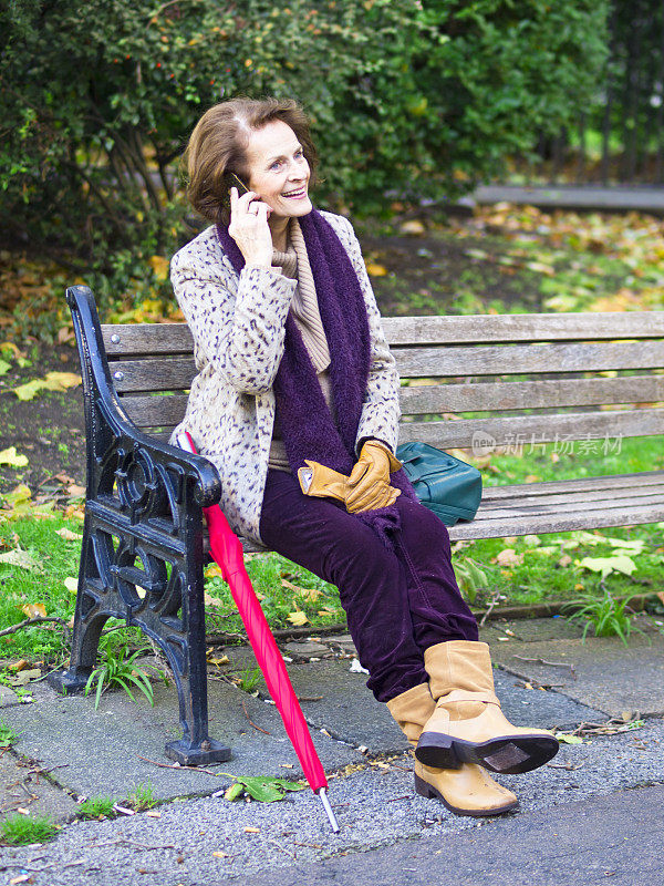 拿着粉红色雨伞的女人坐在公园长椅上玩手机