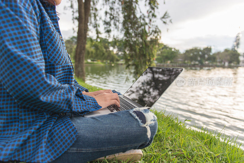 年轻的作家在公园的湖边用笔记本电脑工作