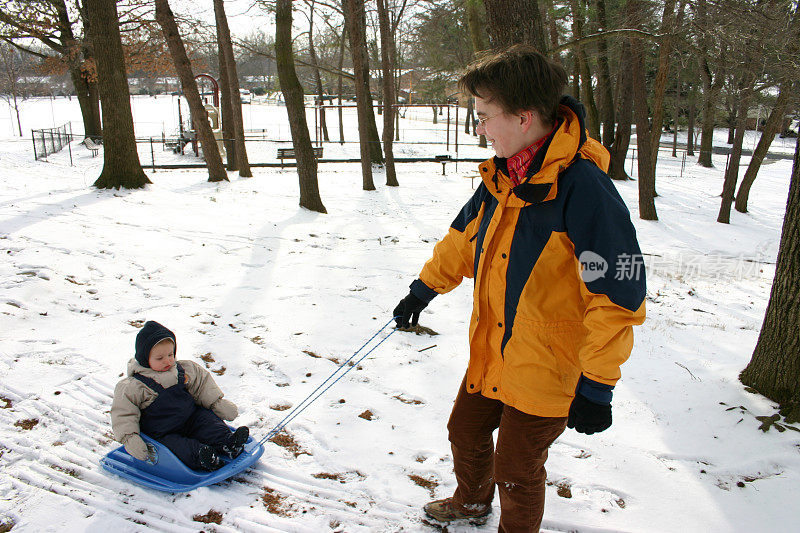 家庭在雪中的乐趣妈妈拉着小女孩在雪橇上