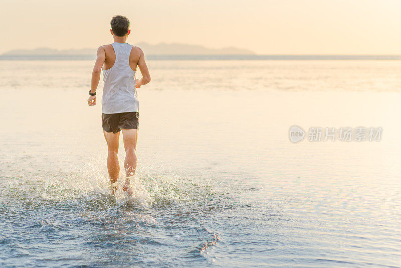 年轻的亚洲男子在海滩上奔跑，夕阳为背景