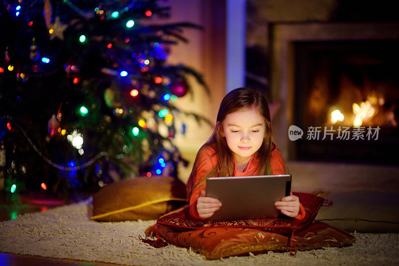 可爱的小女孩在圣诞节壁炉旁使用平板电脑