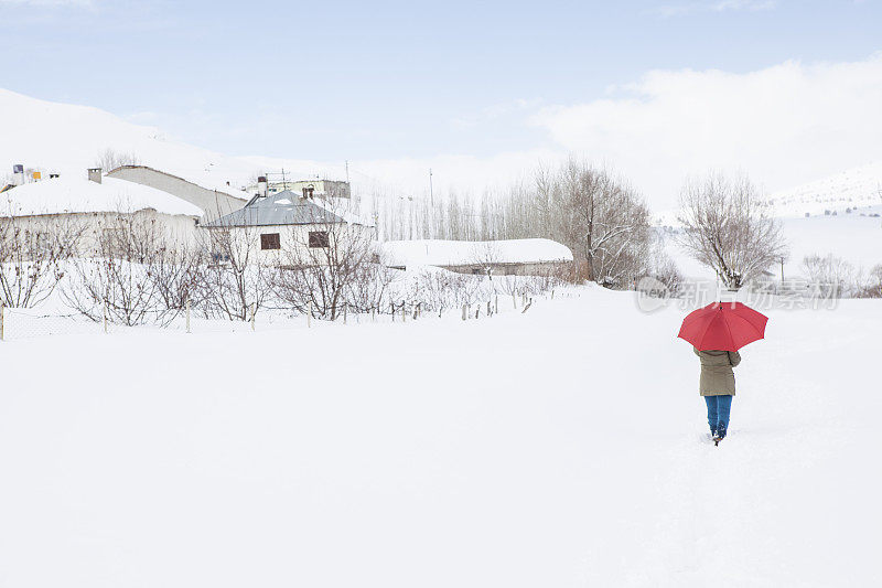 女人撑着红伞走在雪道上