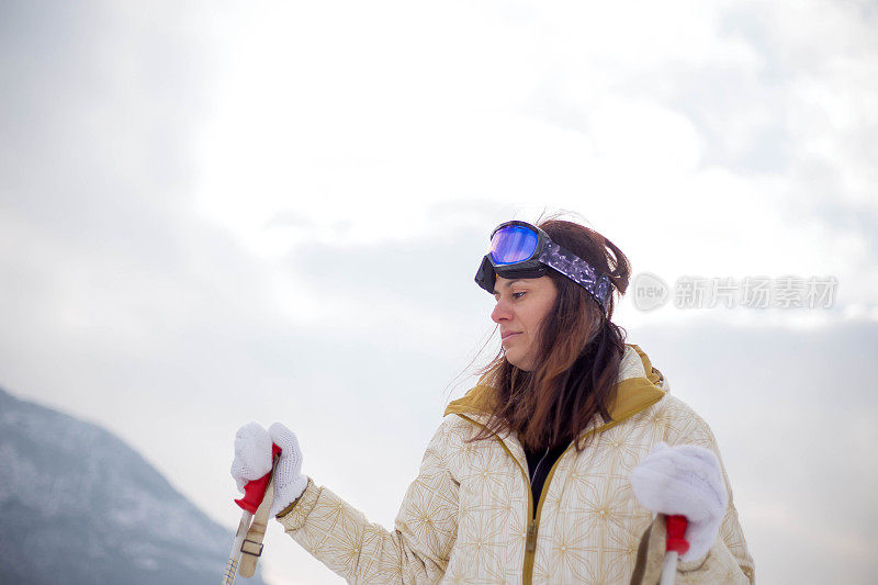 近景美丽的年轻女子在冬天的衣服站在一边，手拿木棍的背景雪山