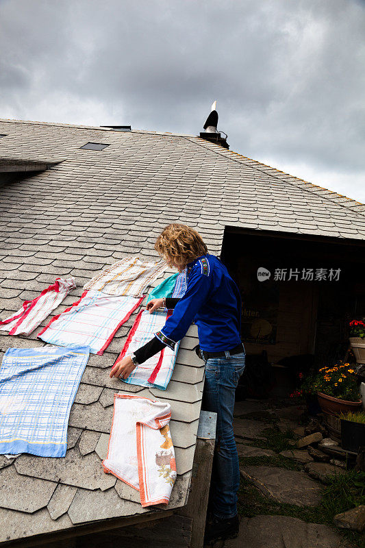 一位瑞士农民的女儿穿着传统服装，在山间小屋的屋顶上晒着毛巾