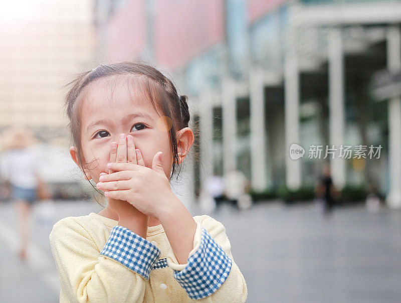 一个亚洲小女孩用手捂住自己的嘴和鼻子。