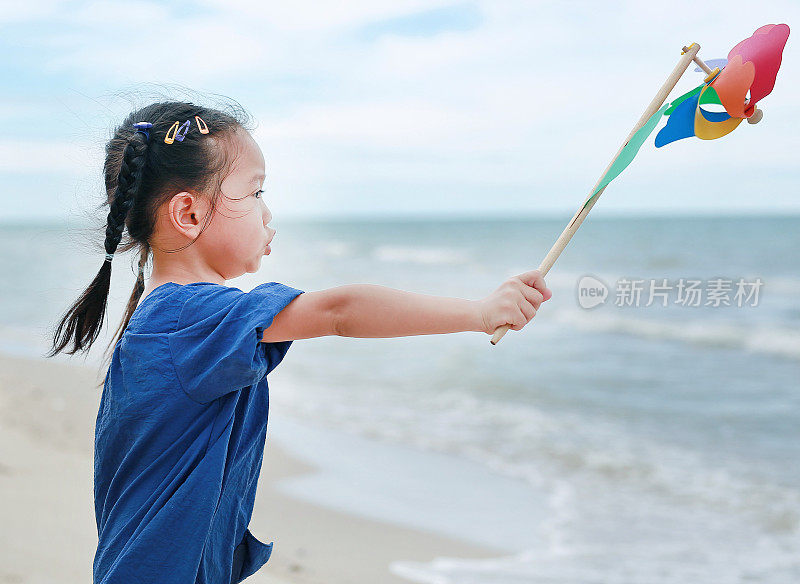 沙滩上的小女孩拿着旋转风车。很酷的基调。