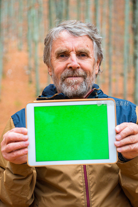 老年男子持有数字平板电脑与绿色屏幕在他的胸前，秋天山毛榉森林，欧洲