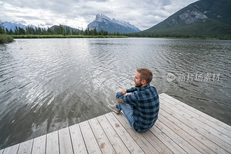 年轻男子在湖码头上看风景