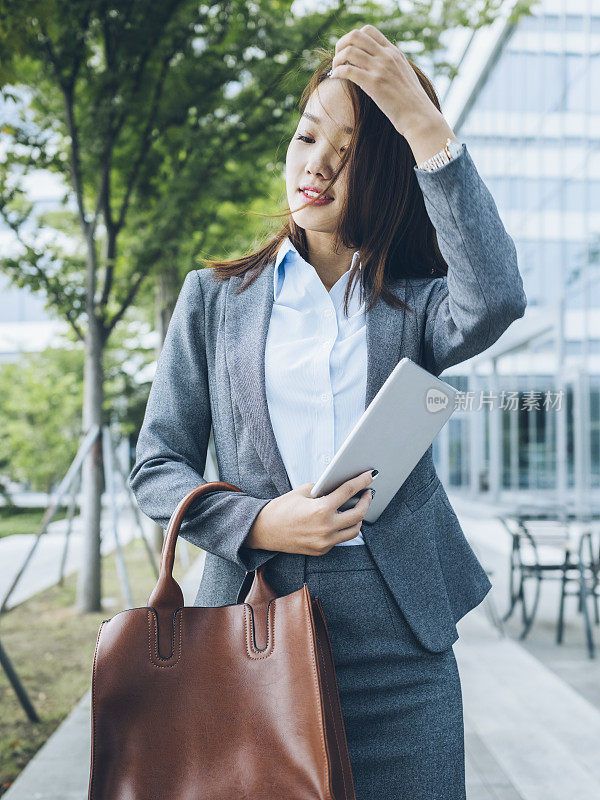 漂亮的亚洲女孩拿着平板电脑走出办公楼