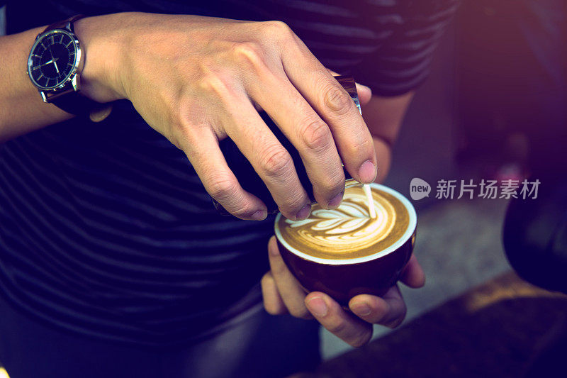 软焦点在咖啡师的表演技巧，以翅膀郁金香图案的拿铁艺术使用无柄水壶。有选择的专注于咖啡师的手倒拉花艺术