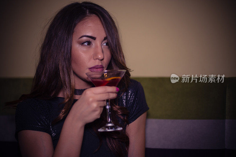 一个年轻漂亮的女人在酒吧喝鸡尾酒的肖像