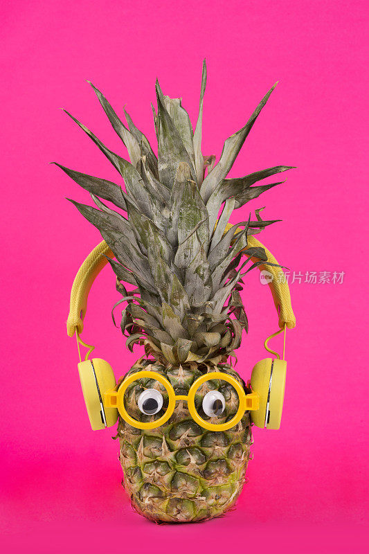 时尚新鲜菠萝与眼镜和耳机在粉红色的背景。