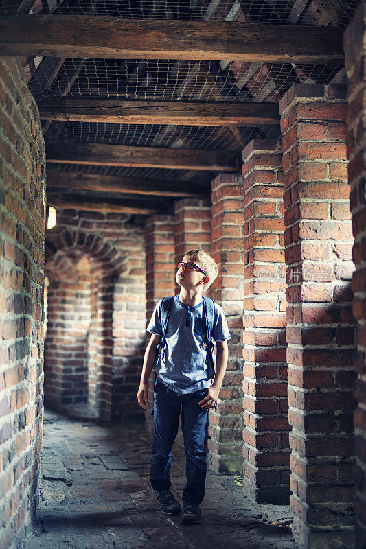 小男孩走在中世纪城墙的走廊上
