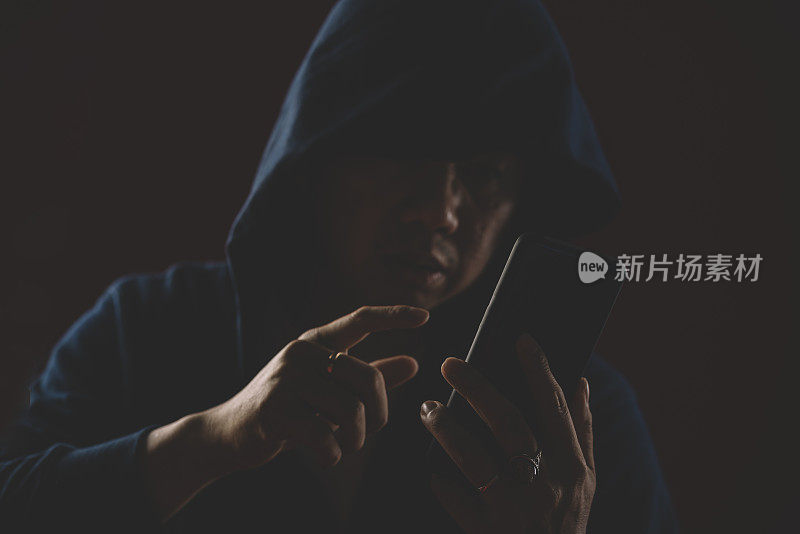 一名穿着连帽衫的亚裔华人男性在黑暗区域使用智能手机