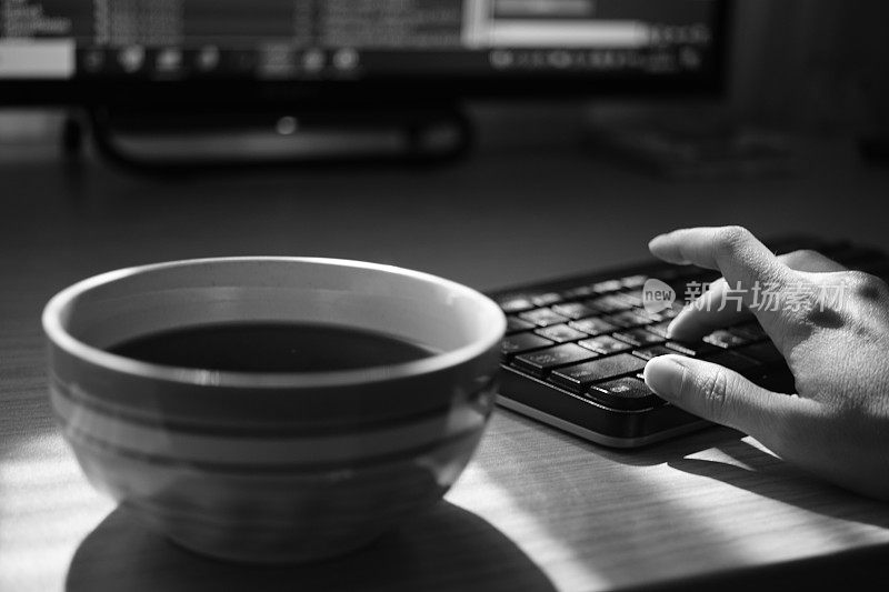 工作场所在办公室的桌子上放上一杯茶和一个键盘，工作环境，选择性聚焦，bw照片
