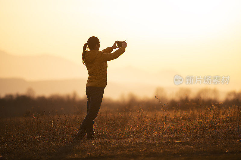 回归自然。一个人用智能手机拍照。一个快乐的年轻女游客漫步在大自然中。户外日落享受。