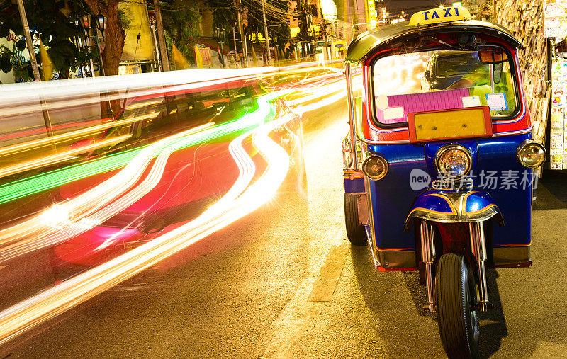 模糊的交通经过一辆停着的嘟嘟车，曼谷，泰国