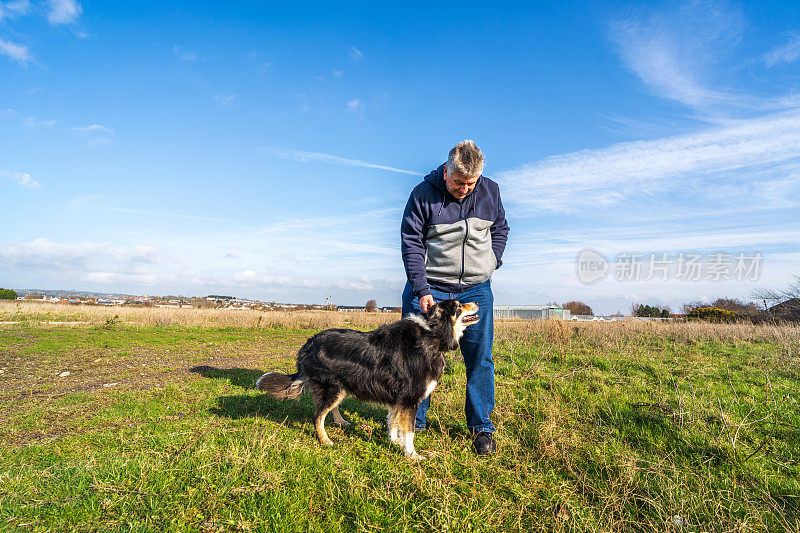 一名男子和边境牧羊犬在草原上散步