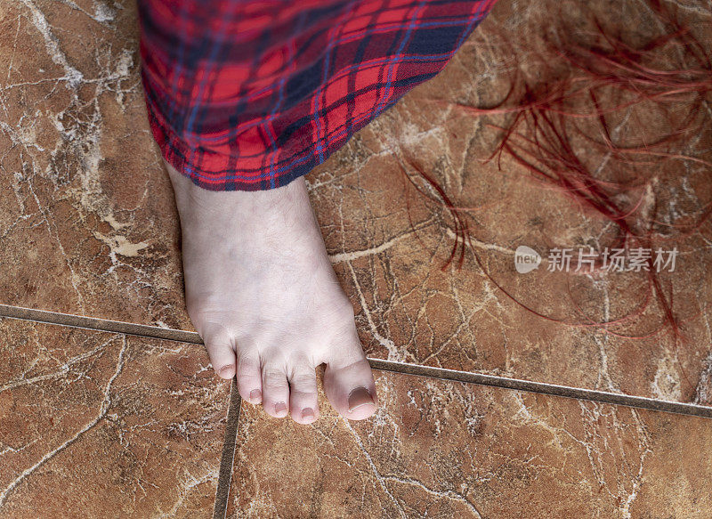 一个十几岁女孩的腿在地板上被剪断的头发覆盖着，正在做一个自制的发型