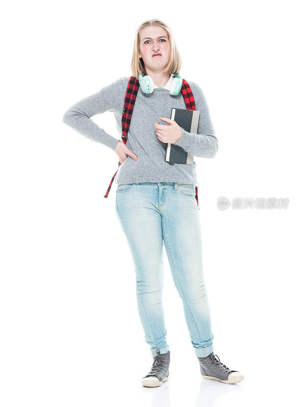 z一代女高中生穿着牛仔裤站在白色背景前，拿着课本，戴着耳机