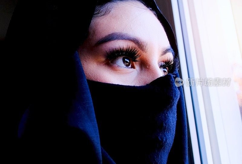 严肃的中东穆斯林年轻女子透过窗户往外看