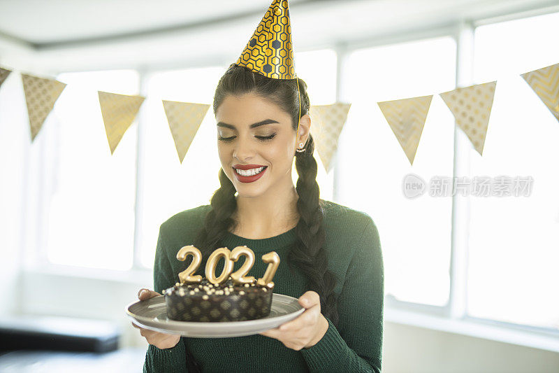 一名年轻女子在家庆祝圣诞节，手里拿着巧克力蛋糕，蛋糕上插着2021年的蜡烛