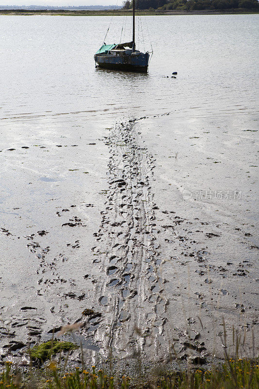 淤泥中的脚印通向河口水中的小船