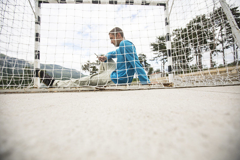 一个年轻人坐在空荡荡的足球场上玩手机
