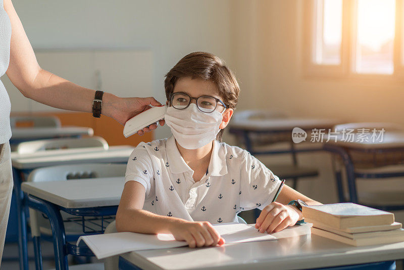 老师用红外线额头体温计检查学童的体温，看有无病毒症状。