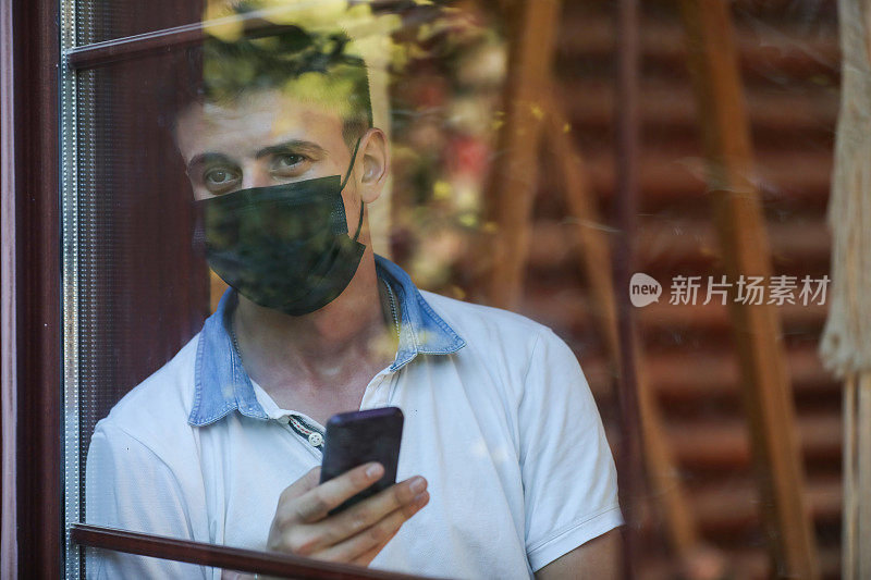 一名被隔离的男子望着窗外，用手机发短信