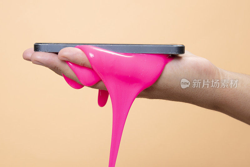女人的手使用智能手机与霓虹粉黏泥玩具在橙色的流行艺术背景。
