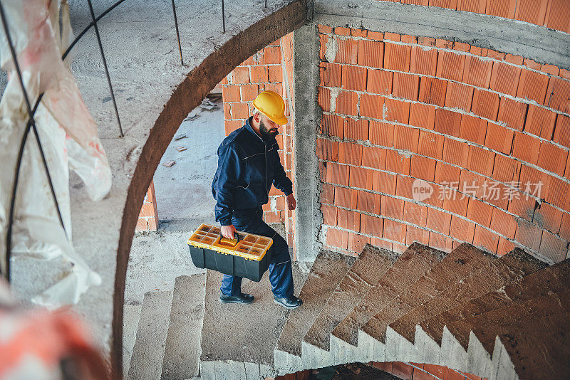 年轻男性建筑工人在建筑工地搬运工具箱