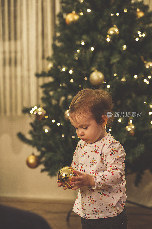 可爱的小女孩在玩一个金色的圣诞装饰品
