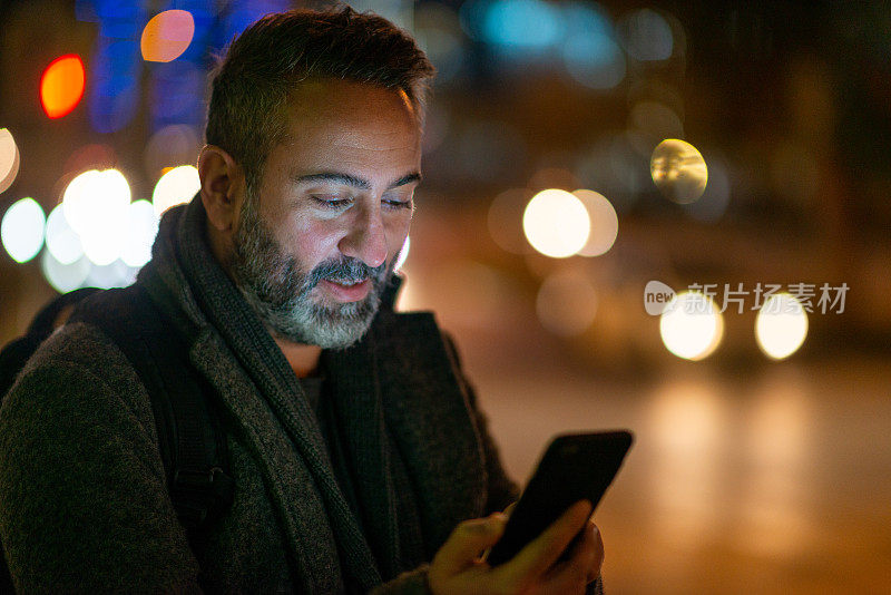 一个男人晚上在街上看智能手机的照片