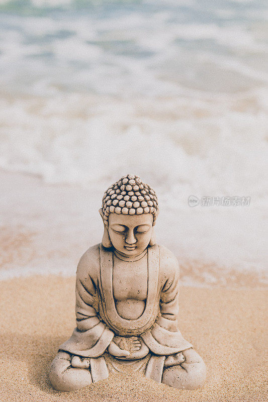 一个佛陀石像的特写与泪滴在脸上坐在海滩上的海滩上从上面稍微拍摄
