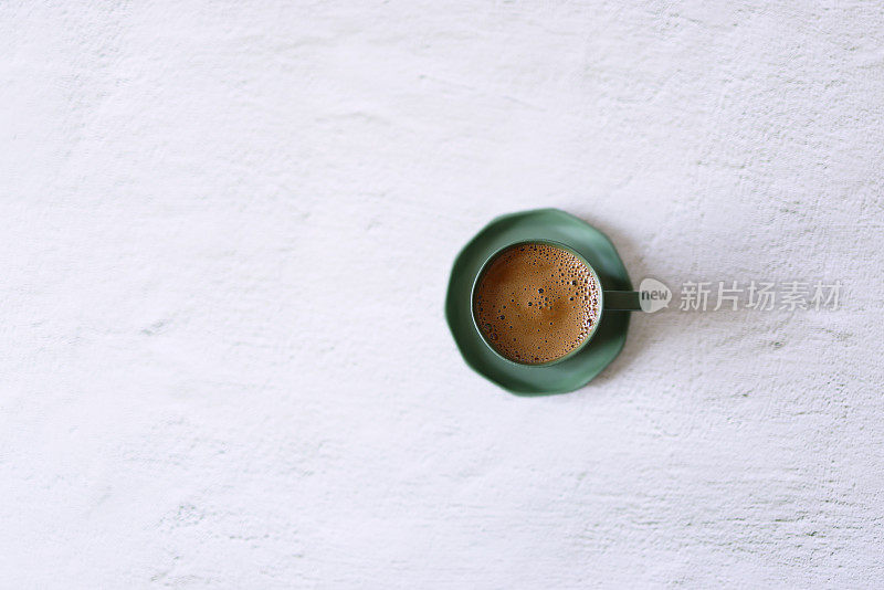 在浅灰色的混凝土地板上，绿色的陶瓷杯里装着起泡的土耳其咖啡
