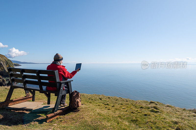 一个活跃的老男人在长凳上用着平板电脑