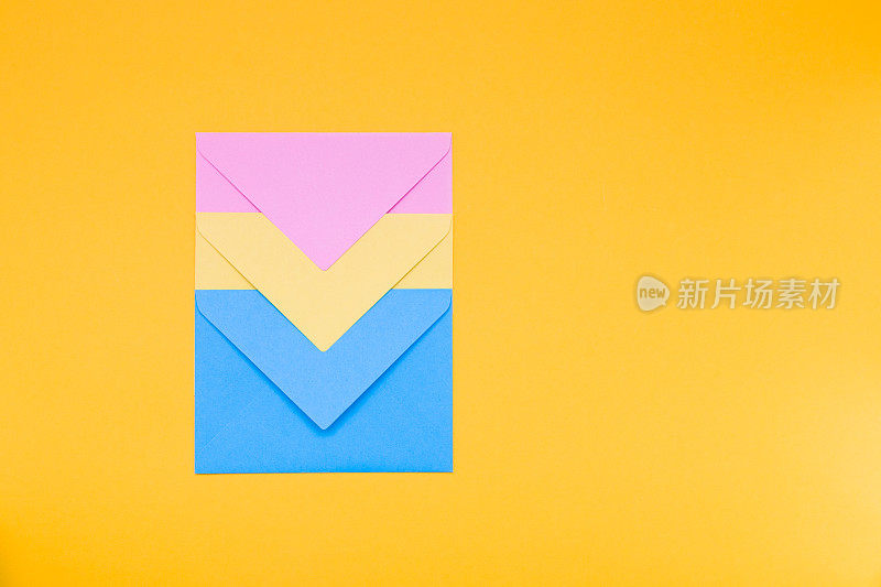 黄、蓝、粉三个颜色相互嵌套的信封躺在一个黄色的背景拷贝空间俯视图上，极简主义的概念为祝贺