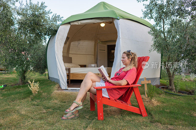 女人在森林里露营，在帐篷前看书。