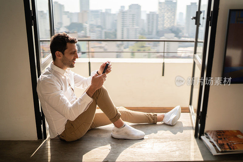 一名男子坐在家里的窗台上使用智能手机