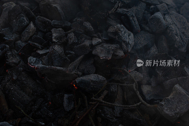 照片在一个黑暗的关键，燃烧和闷烧木炭与最后的火花和烟。