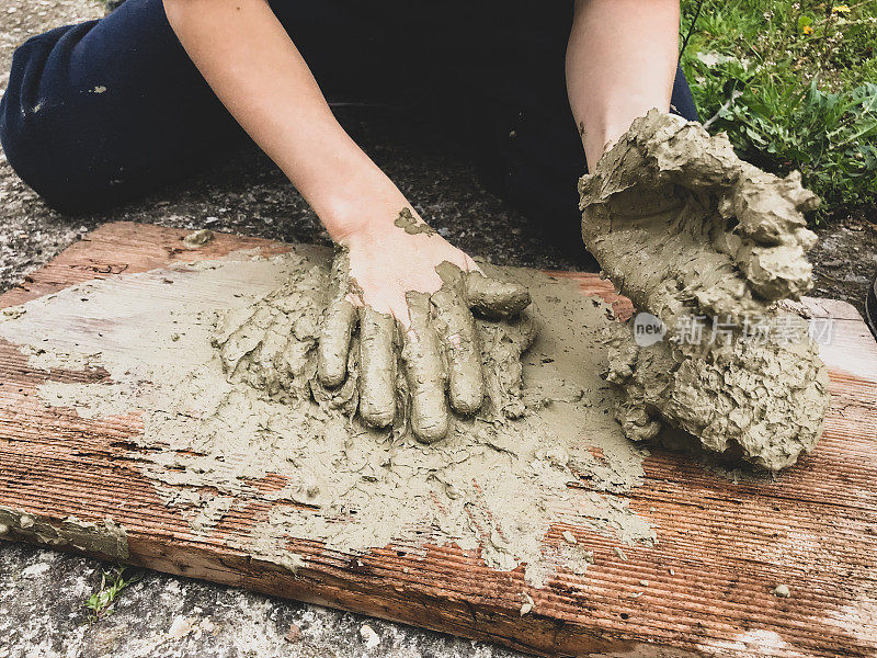 一个孩子在玩潮湿的沙子。一个小孩在地板上的木板上揉捏湿粘土并制作模型。湿砂游戏。